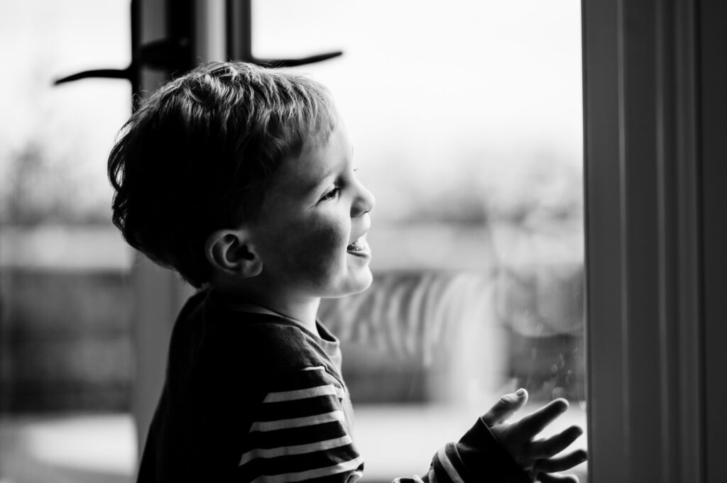 Lifestyle photography of a child looking out at the Rutland countryside from a luxury holiday cabin in black and white