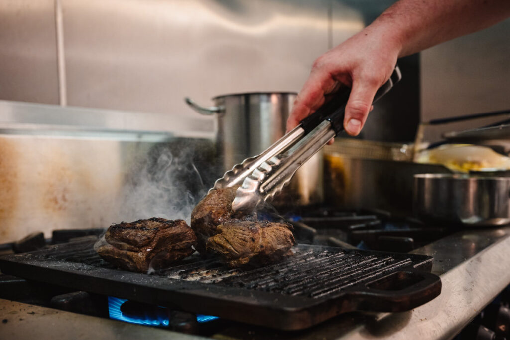 Action shot of a chef searing meat in a professional kitchen for a Leicestershire restaurant branding photoshoot